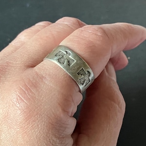 May include: A silver-toned ring with a band design featuring three stylized bird motifs. The ring has a slightly worn appearance, suggesting it is vintage or has been well-loved. The ring is a wide band style.