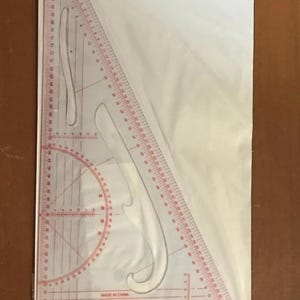 May include: A clear plastic triangle ruler with red markings. It features a protractor, a curved ruler, and a straight ruler. The ruler is labelled "Made in China" and "XITENAITUF No. 3009".