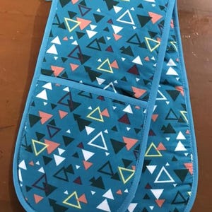 May include: A pair of blue oven mitts with a geometric pattern of triangles in shades of blue, white, yellow, pink, and black.