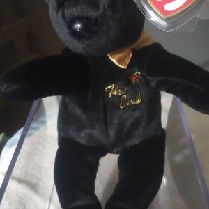 May include: Black Beanie Baby plush bear with a gold collar and "The End" embroidered on the chest. The bear has a red and white Ty tag attached to its ear.