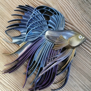 May include: A metallic blue, purple and gold fish sculpture with a detailed, intricate design. The sculpture is made of a material that resembles metal and has a shiny finish.