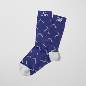 Könnte beinhalten: Ein Paar blaue Socken mit einem sich wiederholenden Muster aus silbernen Sicheln. Die Socken haben weiße Fersen und Zehen, und die Initialen "HS" sind auf den Bündchen gestickt. Der Text "Healthy Socks" ist auf der Unterseite aufgedruckt.