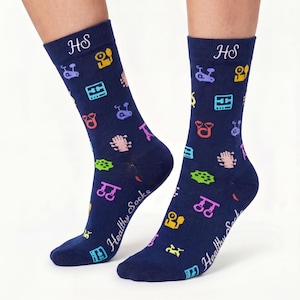 Può includere: Un paio di calzini blu navy con un motivo ripetuto di icone colorate di attrezzature per il fitness. Il bordo superiore mostra le lettere HS ricamate in bianco, mentre il lato del piede presenta la scritta Healthy Socks in bianco.