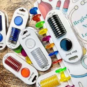 May include: Assortment of colorful plastic disc rings for a binder. The rings are packaged in clear plastic with the text "Disc Ring" and the size "32 MM / 1.25 inch" printed on the packaging.