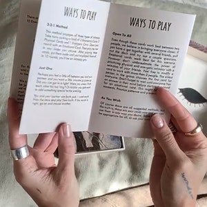 Może przedstawiać: Biała książeczka otwarta na stronie tytułowej z napisem "Ways to Play". Książeczka zawiera instrukcje do gry w karty. Książeczka jest otwarta, aby ujawnić tekst wewnątrz, kt&oacute;ry zawiera r&oacute;żne sposoby gry.