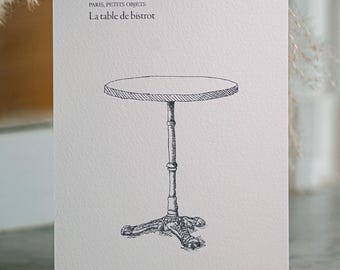 May include: A white rectangular card featuring a black ink line drawing of a round bistro table with a central pedestal base. The text reads PARIS, PETITS OBJETS, La table de bistrot, and at the bottom right, Café d'été, Paris à 30 °C.