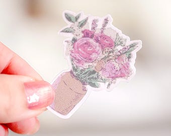 May include: A die-cut sticker featuring a bouquet of pink and purple flowers with green foliage arranged in a tan-coloured vase. The illustration has a textured, vintage-inspired appearance with soft edges and a white border outline.
