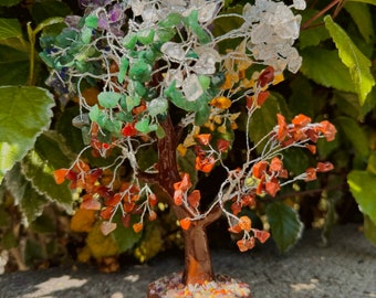 May include: A crystal tree with a brown wooden base. The tree is decorated with various colored crystals, including clear, green, red, orange, and purple.
