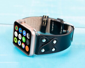 May include: A black leather watch strap with silver studs and a rose gold Apple Watch with a variety of app icons on the screen.