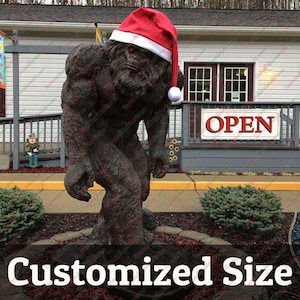 Könnte beinhalten: Eine braune, pelzige Bigfoot-Statue, die einen roten Weihnachtsmann-Hut trägt. Die Statue steht vor einem Gebäude mit einem Schild, auf dem "GEÖFFNET" steht.