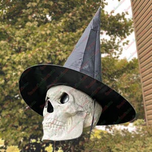 May include: A Halloween decoration featuring a skull wearing a black witch hat. The skull is off-white with dark eye sockets and a prominent nose cavity. The hat has a wide brim and a tall, pointed crown, creating a spooky aesthetic.