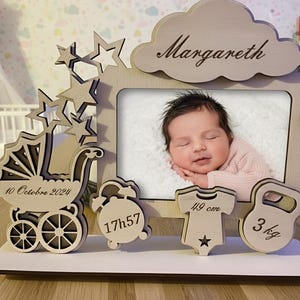 Peut inclure: Cadre photo en bois pour bébé avec le nom "Margareth" gravé sur un nuage. Il contient une photo de bébé, une poussette, des étoiles, et des détails : 10 Octobre 2024, 17h57, 49 cm, et 3 kg.