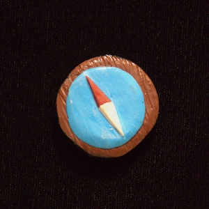 May include: A small, round, blue compass with a red and white needle pointing north. The compass is surrounded by a brown frame.