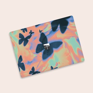Puede incluir: Funda para portátil con un diseño abstracto vibrante. Grandes siluetas de mariposas azul oscuro sobre un fondo arremolinado de tonos naranja, turquesa y amarillo. El logotipo de Microsoft es visible.