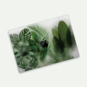 May include: A white laptop skin with a green tropical leaf design. The design features a variety of leaves, including palm leaves, monstera leaves, and other tropical foliage. The leaves are arranged in a random pattern and are semi-transparent, giving the skin a subtle and elegant look.