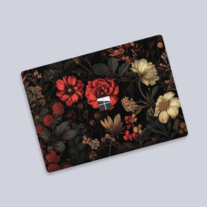 May include: A laptop skin with a dark background and a floral pattern featuring red, white, and yellow flowers. The flowers are arranged in a repeating pattern and are surrounded by green leaves.