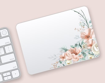 May include: A rectangular white mousepad with rounded corners, featuring a floral design in the upper right corner. The flowers are peach and white, with green leaves and stems. A silver keyboard is in the lower left corner.