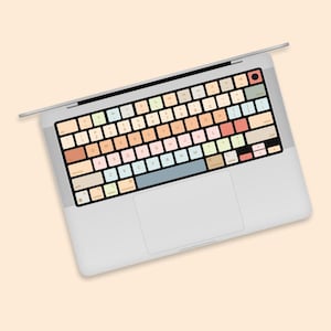Peut inclure: Un ordinateur portable argenté avec un jeu d'autocollants de clavier colorés. Le clavier présente une variété de couleurs pastel et comprend des lettres, des chiffres et des symboles.