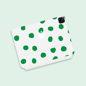 May include: White phone case with a green polka dot pattern. The case has a cutout for the camera lens and a white Apple logo.