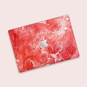 May include: A red and white laptop case with a marble design. The case has a cutout for the Apple logo and a glossy finish. The design features a mix of red hues with white veins and speckles.