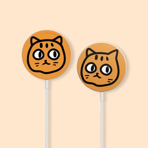 May include: Two orange wireless charging pads with a black outline of a cat face on each. The cat faces have black eyes and whiskers.