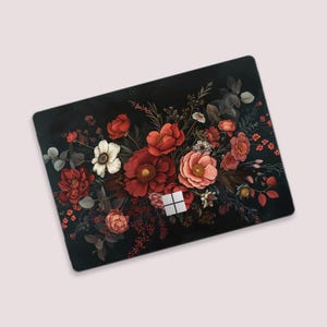Puede incluir: Una funda para portátil negra con un diseño floral. El diseño incluye flores rojas, rosas y blancas con follaje verde. El logotipo de Microsoft es visible. La estética general es oscura y romántica.