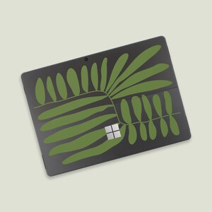 May include: A black laptop with a green leafy design. The laptop has a small white square in the centre of the keyboard.