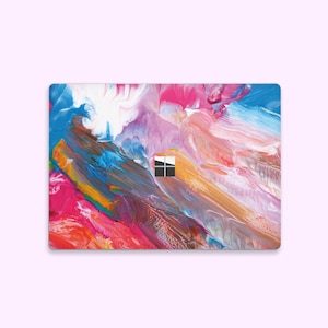 Peut inclure: Peau d'ordinateur portable avec un design abstrait coloré, présentant des coups de pinceau rose, bleu, blanc, jaune et marron. La peau a une découpe pour l'appareil photo de l'ordinateur portable et une petite découpe carrée pour le logo Windows.
