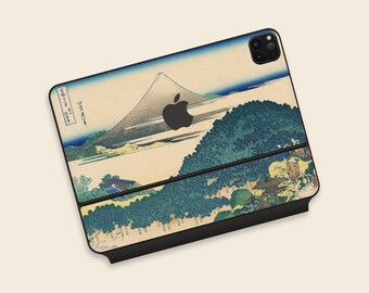 May include: An Apple iPad Pro with a decorative skin featuring a Japanese landscape painting. The skin showcases a mountain, trees, and a river in shades of blue, green, and beige. The Apple logo is visible.