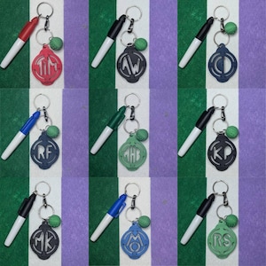 May include: Nine keychains with a black and white dry erase marker attached to each. Each keychain has a green, blue, or red circle with a white monogram in the center. The circles are attached to a silver key ring.