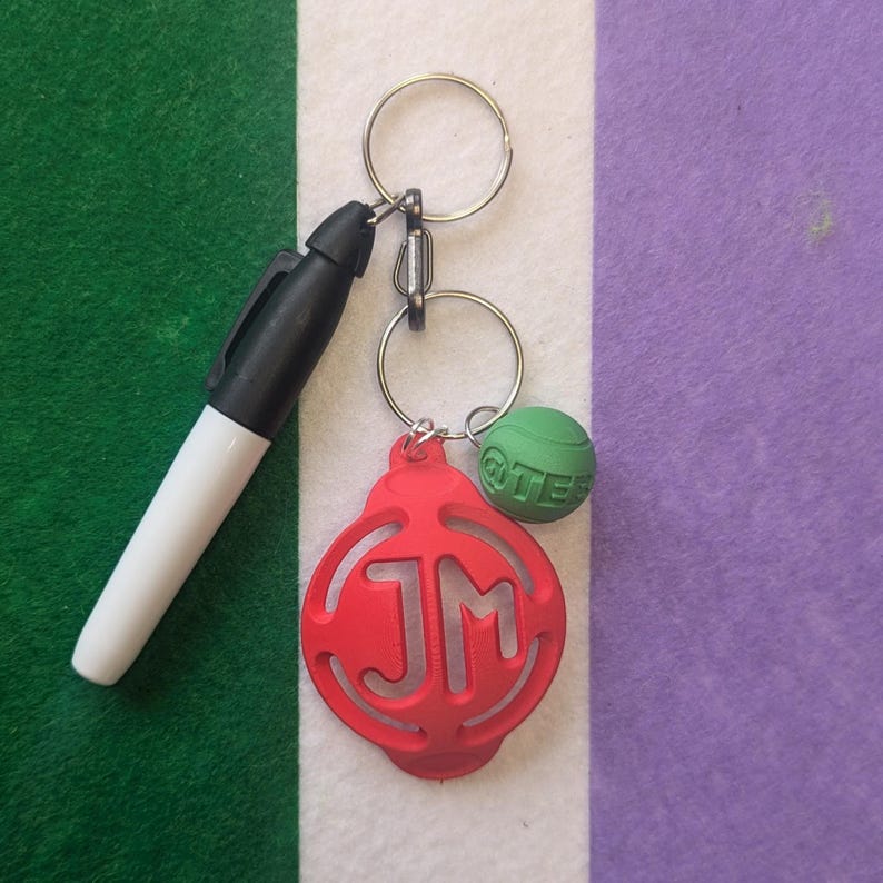 May include: A red keychain with the initials "JM" in a circle design. The keychain is attached to a silver key ring with a green ball charm that says "QUIET" on it.
