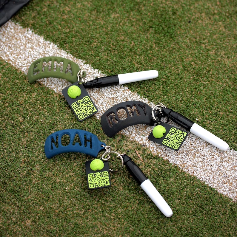 May include: Three personalized keychains featuring curved silicone name tags in olive green, black, and blue. Each keychain includes a small black and white marker, a lime green ball accent, and a square black tag with a lime green QR code.
