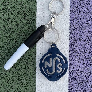 May include: A blue keychain with the letters "NS" in a circle design. The keychain is attached to a silver key ring and a white dry-erase marker.