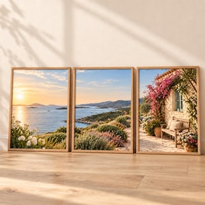 May include: A set of three framed wall art prints featuring Mediterranean coastal scenes. Two prints display a sunset over the sea with rocky hills and vegetation, while the third shows a stone building with a wooden bench and pink flowers.