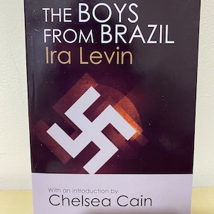 May include: A book cover with a black background and white text that reads "The Boys From Brazil" by Ira Levin. The cover also features a white swastika symbol and the text "With an introduction by Chelsea Cain".