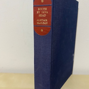 Peut inclure: Un livre relié de couleur bleu marine avec un dos rouge et des lettres dorées. Le titre est "South by Java Head" par Alistair MacLean.