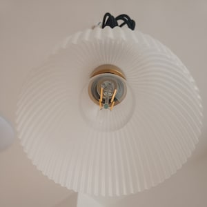Op de afbeelding: Witte, geplooide glazen lampenkap met een gouden fitting en een heldere gloeilamp.