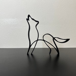 Könnte beinhalten: Eine schwarze Metallskulptur eines Wolfes, der zum Mond heult. Die Skulptur ist aus dünnem Draht gefertigt und sehr detailliert.