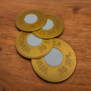 May include: Four gold-coloured .38 Special Winchester bullet casings stacked on top of each other on a wooden surface.