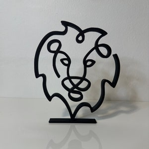 Può includere: Scultura in metallo nero di una testa di leone, realizzata con un'unica linea continua. La scultura è montata su una base nera.