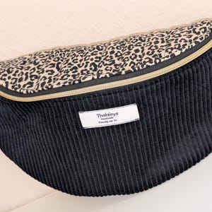 Könnte beinhalten: Schwarze Cord-Bauchtasche mit einem Oberteil mit Leopardenmuster und einem goldenen Reißverschluss. Die Tasche hat ein Etikett mit dem Text "Thalainys Handmade".