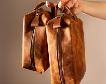 May include: Two brown leather zippered travel bags with a distressed look.