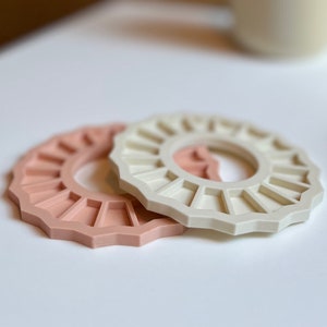 May include: Two silicone rings, one in a light pink colour and the other in a cream colour. The rings are shaped like a sun with a hole in the centre.