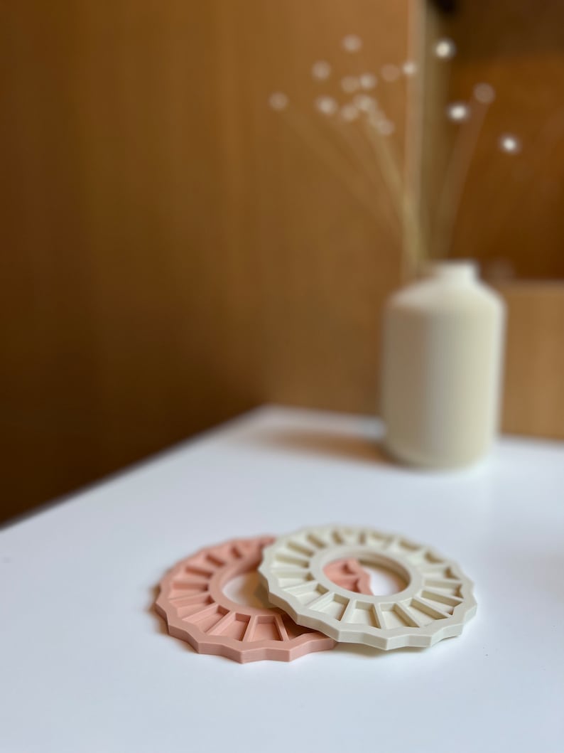 May include: Two silicone rings, one in a light pink colour and the other in a cream colour. The rings are shaped like a sun with a hole in the centre.