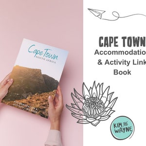 May include: A closed book with a photograph of a mountain range on the cover. The cover is titled "Cape Town South Africa" and has the text "Accommodation & Activity Link Book". The book is being held by a person's hands.