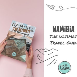 May include: A travel guide book with the title "Namibia The Ultimate Travel Guide" by Kim and Wayne. The cover features a photo of a car driving on a road with a map in the foreground.