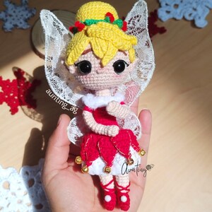 May include: A crocheted fairy doll with blonde hair, a red dress, white wings, and gold bells. The doll is wearing red shoes and has a green holly wreath around her head.