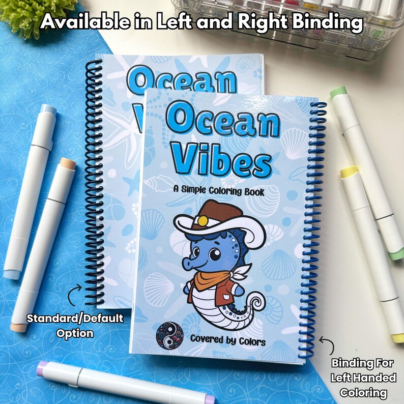 May include: Two spiral-bound coloring books titled "Ocean Vibes" with a seahorse illustration. The books are light blue with white text and illustrations. Several white markers with colored tips are scattered around the books. Text on the books reads "A Simple Coloring Book".