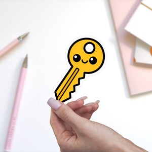 May include: A yellow key sticker with a cartoon face featuring two black circular eyes and a small curved mouth. The key has a circular hole at the top and a jagged edge along the bottom, outlined in black with a white border against a plain background.