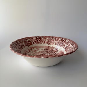 Może przedstawiać: Biała ceramiczna miska z bordowym wzorem kwiatowym i krajobrazowym na obrzeżu. Miska ma falisty brzeg i prosty, zaokrąglony kształt. Wnętrze miski jest białe.